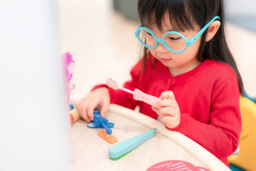 A young girl is sitting at a table with a variety of toys, including a set of doctor's tools. She is smiling and she is enjoying herself