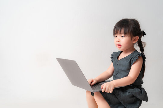 Asian girl using a laptop indoors. She is focused on the screen, pointing with her finger while sitting against a plain white background.