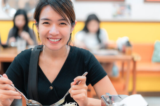 A woman is smiling while eating at a restaurant. She is holding a fork and spoon in her hands