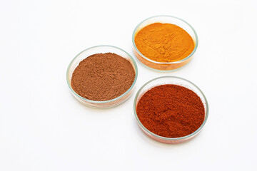 Turmeric powder, paprika (ground red pepper) and cinnamon powder in a petri dish, white background