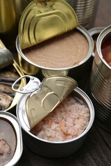 Open tin cans with different preserved products on wooden table, closeup