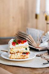a piece of cake with buttercream on pieces of multi-colored jelly on a white saucer on a wooden tray under the sun's rays, espresso coffee in a white cup, a transparent teapot with coffee, flowers