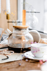 espresso coffee in a white cup on a white saucer on a wooden tray under the sun's rays, a transparent teapot with coffee, flowers, a book, morning coffee, drink, light composition, still life