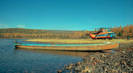 Obraz premium Homemade boat with an outboard motor and Soviet helicopter in upper reaches of Siberian river in autumn.