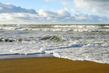 Scenic Baltic sea coastal seascape, stormy sea with big foamy waves, cloudy blue sky, sandy beach