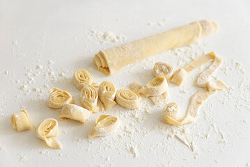 Preparing homemade tagliatelle pasta on on white table: cutted roll of dough. Top view