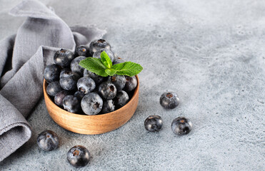 Wooden bowl of fresh blueberries with mint leaves on blue background.