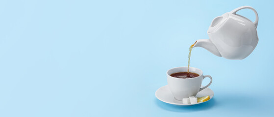 Pouring of hot tea from teapot into cup on color background