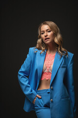Beautiful stylish woman in a blue suit with flowers photo shoot on a black background. Charming blonde smiling posing in front of the camera