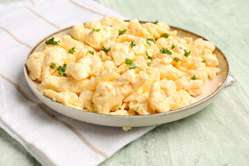 Plate of scrambled eggs with napkin on green wooden background