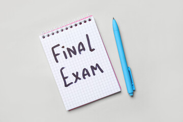Notebook with text FINAL EXAM and pen on grey background