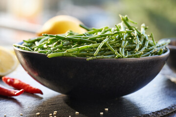 Fresh Salicornia seaweed in a bowl with sesame seeds, chilli peppers and lemon