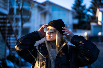 Cozy girl basking in winter sun. A young woman stands outside in winter, wearing a warm jacket,...