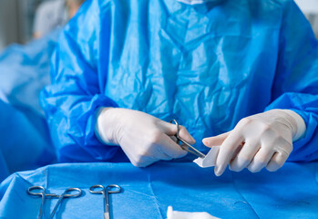 Team readies tools for surgery. A healthcare professional in blue scrubs uses scissors to prepare sterile instruments before a surgical procedure.