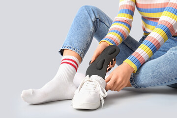 Young woman sitting and putting orthopedic insoles in sneakers isolated on white background