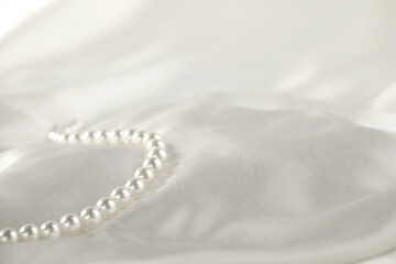 Beautiful pearl necklace on white silk, closeup. Space for text
