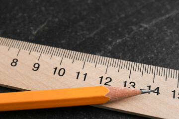 Wooden ruler and pencil on black table, closeup