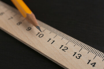 Ruler and pencil on black wooden table, closeup