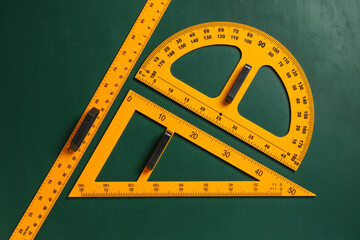 Triangle, protractor and ruler on green chalkboard, flat lay