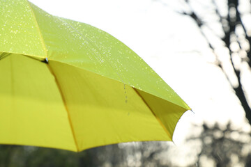 Open yellow umbrella under pouring rain outdoors, closeup. Space for text