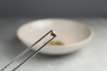 Tweezers with gold nugget against blurred background, closeup. Space for text