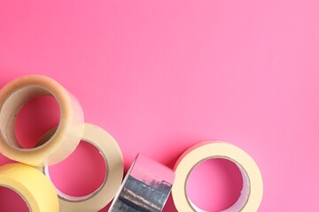 Rolls of different adhesive tapes on pink background, flat lay. Space for text