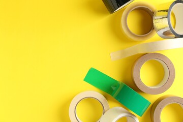 Rolls of different adhesive tapes on yellow background, flat lay. Space for text