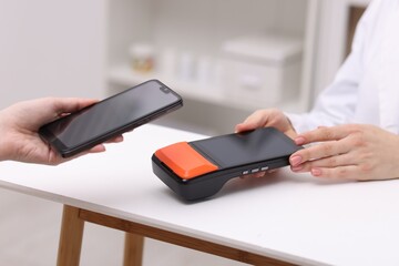 Woman paying with smartphone via terminal at counter indoors, closeup