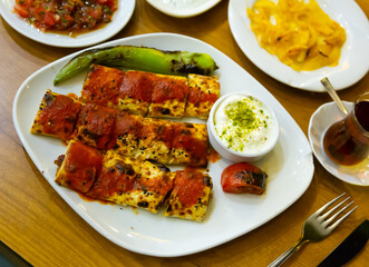 Portion of beyti kebab served on plate with grilled vegetables and yogurt.