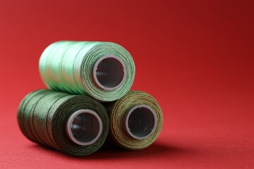 Spools of colorful sewing threads on red background, closeup. Space for text
