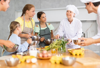 Children are excited to learn how to beat raw eggs with whisk under the guidance of a female chef