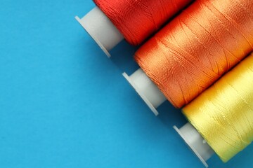 Different spools of sewing threads on light blue background, flat lay. Space for text