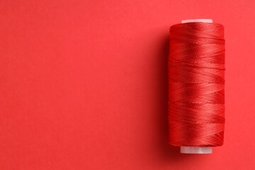 Spool of sewing thread on red background, top view. Space for text