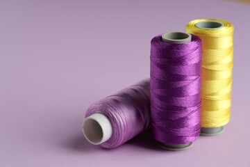 Different spools of sewing threads on violet background, closeup. Space for text
