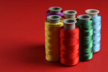 Different spools of sewing threads on red background, closeup. Space for text