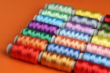 Different spools of sewing threads on orange background, closeup