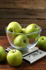 Electronic kitchen scale with bowl of green apples on wooden table, closeup