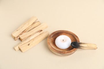 Palo santo sticks, burnt one and burning candle on beige background, closeup