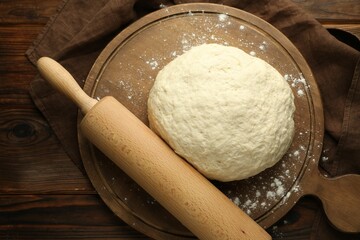 Fresh dough and rolling pin on wooden table, top view