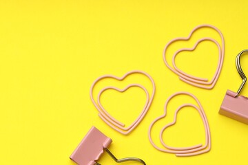 Heart shaped paper and binder clips on yellow background, flat lay. Space for text