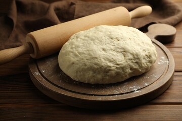 Fresh dough and rolling pin on wooden table, closeup
