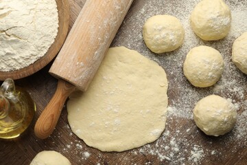 Fresh dough, rolling pin, flour and oil on wooden table, flat lay