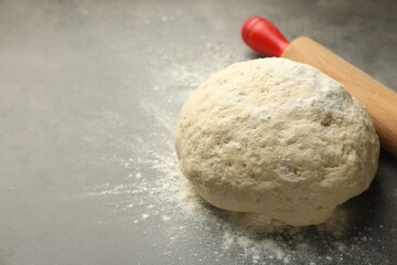 Fresh dough and rolling pin on grey table, closeup. Space for text