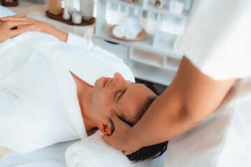 Caucasian man enjoying relaxing anti-stress head massage and pampering facial beauty skin recreation leisure in dayspa modern light ambient at luxury resort or hotel spa salon. Quiescent
