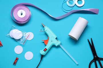 Hot glue gun and handicraft materials on light blue background, flat lay