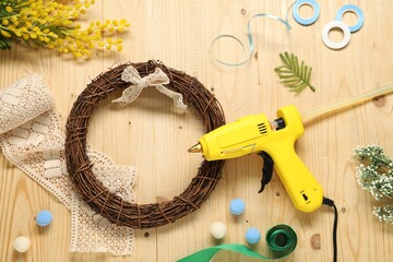Hot glue gun and handicraft materials on wooden background, flat lay