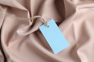 Blank tag with string on beige fabric, closeup