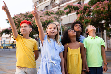 Inquisitive carefree tweens spending time outdoors together during summer vacations, looking up at sky and pointing at something ..