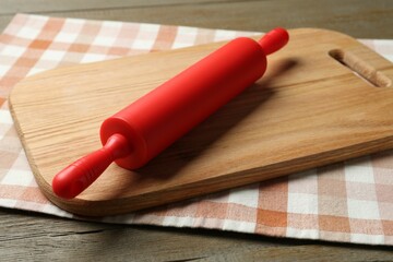 Red rolling pin and board on wooden table, closeup
