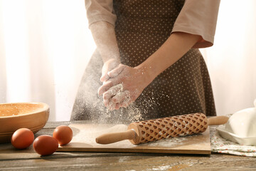Woman with flour and rolling pin at wooden table indoors, closeup